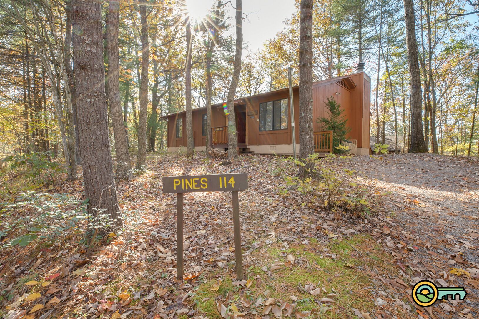Une cabane portant l’inscription « Pines 114 », située dans une zone boisée et accessible par une allée de gravier.