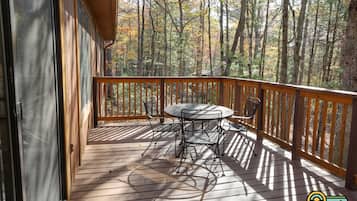 A wooden deck with a table and chairs, overlooking a forested area.