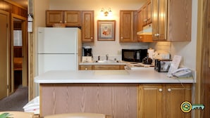 Una cucina compatta con mobili in legno, un frigorifero, un forno a microonde, un tostapane e un lavello.