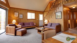 A cozy living room with wooden walls and floors, two purple sofas, a wooden coffee table, and a staircase leading to another level. - Mountainside Chalet (#141A) - Close to Resort lodge | Great view of valley & golf course! (Basye)