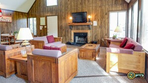 A cozy, wood-paneled living room with a fireplace, comfortable seating, and large windows. - Golf-lover's Mountain Chalet (#150A) - Great view of golf course! (Basye)