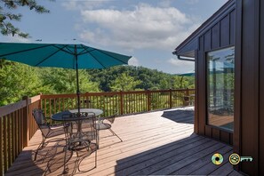 A wooden deck with a table and chairs, a large umbrella, and a view of a forested area.