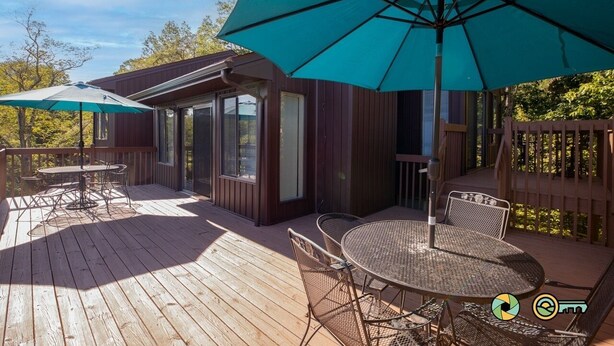 Una terraza de madera con una mesa, sillas y un parasol grande, además de un edificio con ventanas.