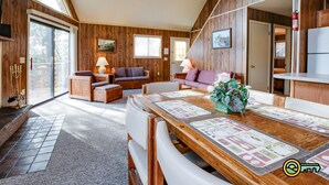 A cozy living room with wooden walls, a dining table with placemats, and a fireplace.
