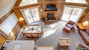 A cozy cabin with a fireplace, wooden walls, a dining area, and a seating area with a TV.