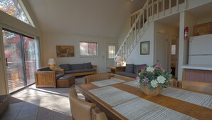 Un salon spacieux avec une table à manger en bois, des sièges confortables et un escalier menant à l’étage supérieur.