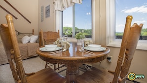 A dining area with a round wooden table set for four, surrounded by wooden chairs. A bed with a beige quilt and white pillows is visible in the background. - Logan Lodge (Unit #135) | Ski/MTB/Golf | Ski slope & Resort valley views | Vaulted ceilings! (Basye)