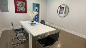 Un comedor moderno con una mesa blanca, cuatro sillas y un jarrón con flores blancas.