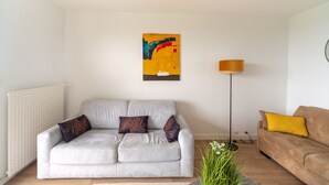Een woonkamer met een grijze bank, een bruine bank, een vloerlamp en een schilderij aan de muur.
