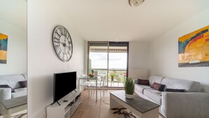 Een moderne woonkamer met een flatscreen televisie, een grote wandklok, een eethoek met tafel en stoelen, en een balkon met uitzicht.