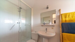 Een badkamer met een douchecabine van glas, een witte wastafel en een toilet.