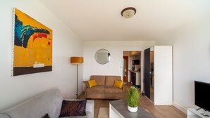 Een moderne woonkamer met een grijze bank, een bruine bank met gele kussens, een salontafel, een televisie, een schilderij en een spiegel.