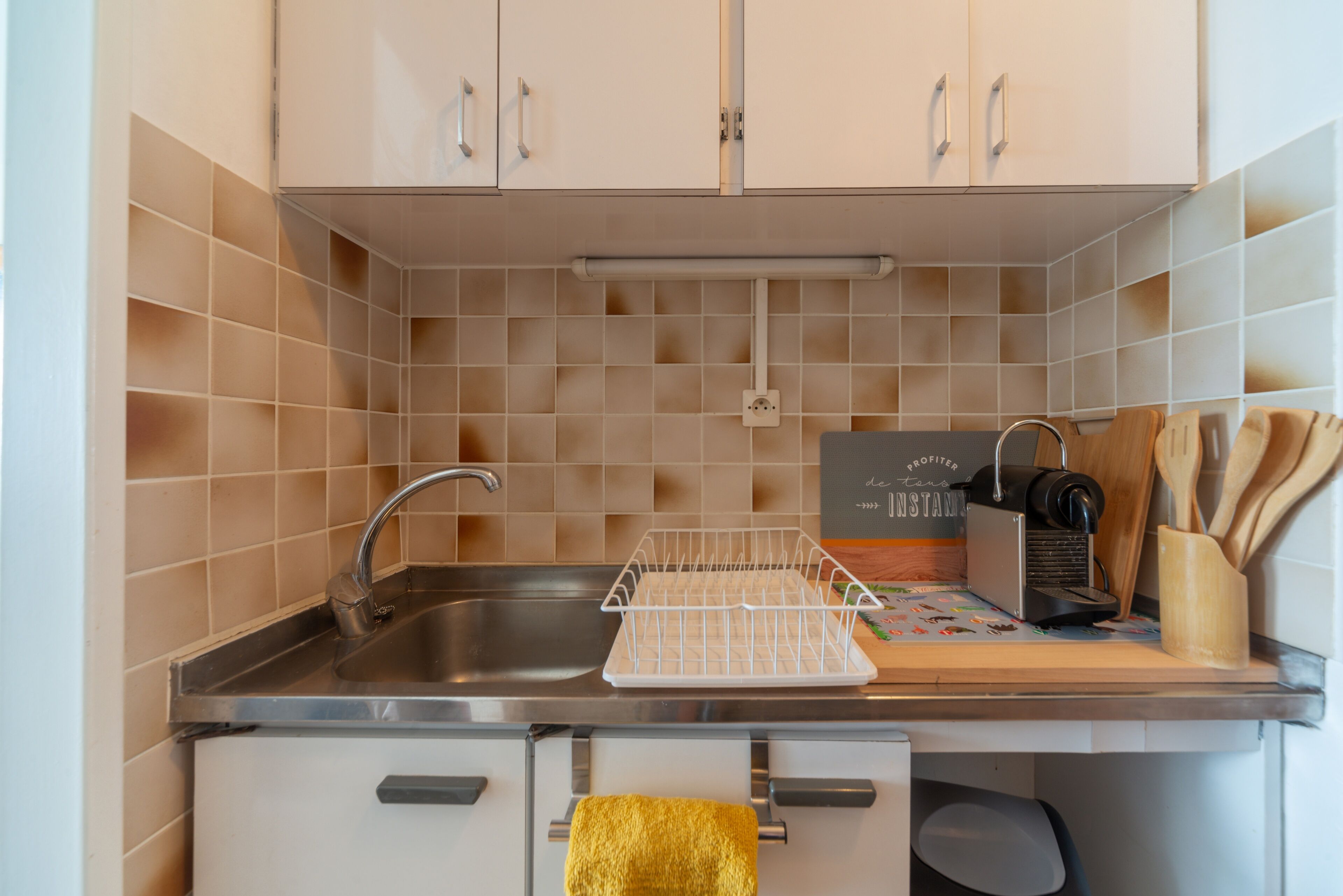 A kitchen with a stainless steel sink, a drying rack, a coffee machine, and wooden utensils on the counter.