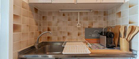 A kitchen with a stainless steel sink, a drying rack, a coffee machine, and wooden utensils on the counter.