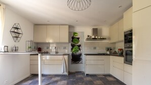 A modern kitchen with white cabinets, a central island, a tiled floor, and a hanging plant. - Dorlanne - One Bedroom House, Sleeps 2 (Saint-Palais)
