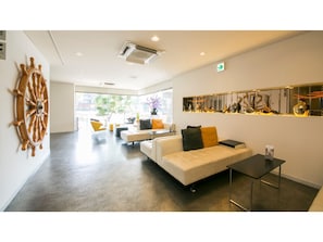 A modern lobby with a large wooden ship wheel, a sofa with cushions, a coffee table, and a wall-mounted display of decorative items.