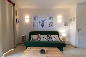 Un salon chaleureux avec un canapé vert, une table basse en bois et des œuvres d’art murales comprenant des motifs d’animaux et une représentation d’un cerf.