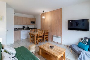 Un espace de vie compact comprenant un coin cuisine, un coin repas et un téléviseur fixé au mur.