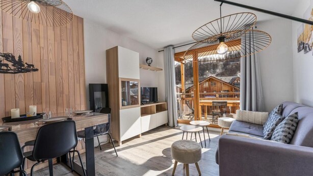 Una sala de estar moderna con un sofá, un comedor con mesa y sillas, y una cocina con televisor y armarios.