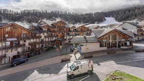 Un hilero de chalets de madera con balcones, un cartel que dice 'Le Parades des Arbres' y una furgoneta blanca estacionada al frente.
