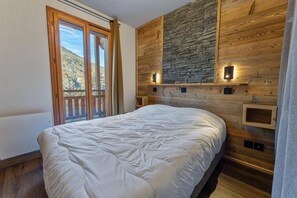 Un dormitorio con una cama grande, paneles de madera en la pared, una pared decorativa de piedra y un balcón con vistas.
