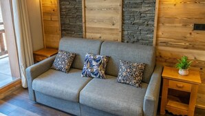 A grey sofa with floral cushions, a small wooden nightstand, and a potted plant. - 150m from ski slopes, 7th floor, view terrace, swimming pool, sauna, terrace, balcony, ski locker (Les Orres)