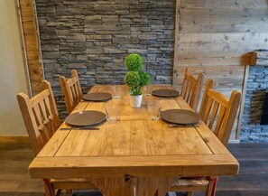 Una mesa de comedor de madera dispuesta para seis comensales, con sillas a juego, una pequeña planta en maceta y vasos de vidrio.