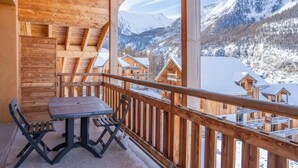 A wooden balcony with a table and chairs, overlooking snow-covered mountains and buildings. - 150m from ski slopes, 7th floor, view terrace, swimming pool, sauna, terrace, balcony, ski locker (Les Orres)