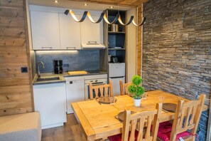 Una cocina compacta con armarios blancos, horno empotrado y pared de piedra.