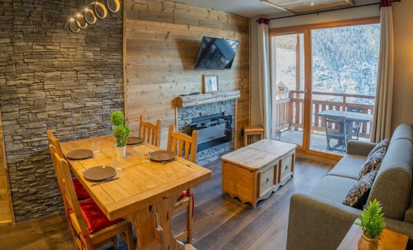 Una sala de estar acogedora con pared de piedra, muebles de madera, chimenea y televisor montado en la pared.