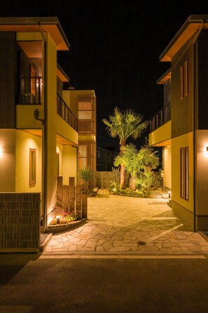 Un edificio moderno con un patio interior de noche, que incluye una palmera y un sendero de piedra.
