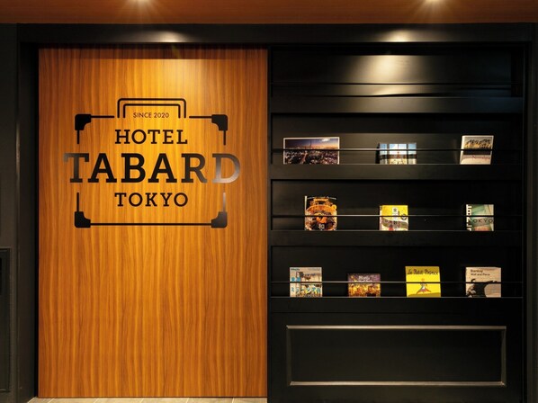 Un mur en bois sur lequel on peut lire l’inscription « HÔTEL TABARD TOKYO », et une étagère avec des livres et des cartes postales.