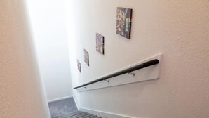Una escalera con barandilla, escalones alfombrados y tres obras de arte enmarcadas en la pared.