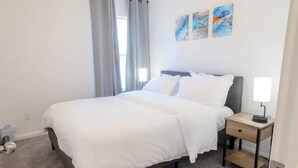 Un dormitorio con cama, mesita de noche y ventana con cortinas.
