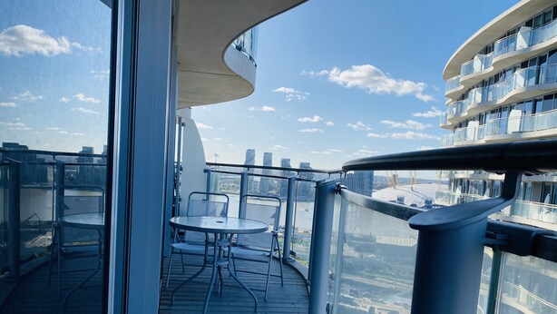 Un balcón con mesa y sillas, vistas a la ciudad y barandilla de cristal.