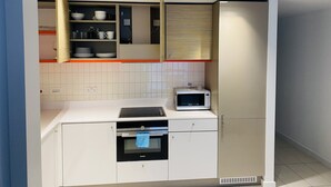 Una cocina moderna con armarios blancos, horno empotrado, microondas y repisas con vajilla.