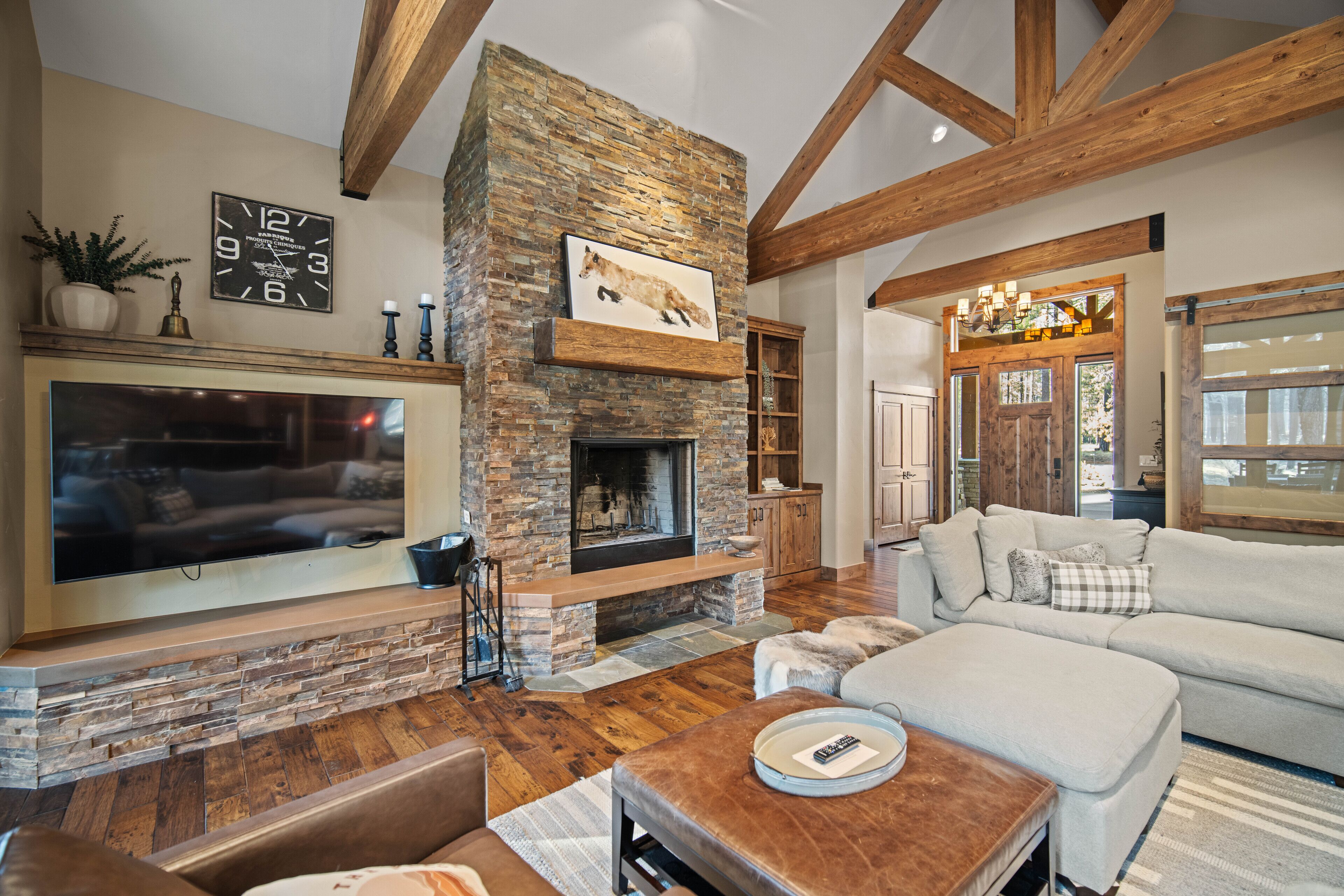 A living room with a stone fireplace, wooden beams, a large TV, and a white sofa.