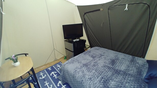Een kamer met een bed, een klein bureau met stoel, een televisie en een gordijn.