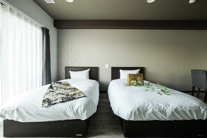 Une chambre d’hôtel avec deux lits simples, une grande fenêtre avec des rideaux, une chaise et un mur orné d’un motif texturé.