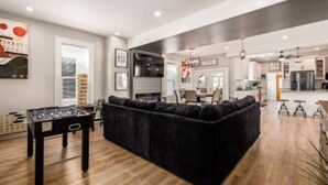 A spacious living area with a dark-colored sofa, a foosball table, and a kitchen in the background.