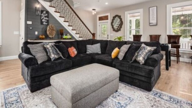 A modern living room with a dark sectional sofa, a grey ottoman, and a patterned rug.