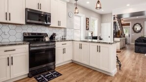 A modern kitchen with white cabinets, a black stove, and a microwave. There is a wooden floor and a rug in front of the stove.