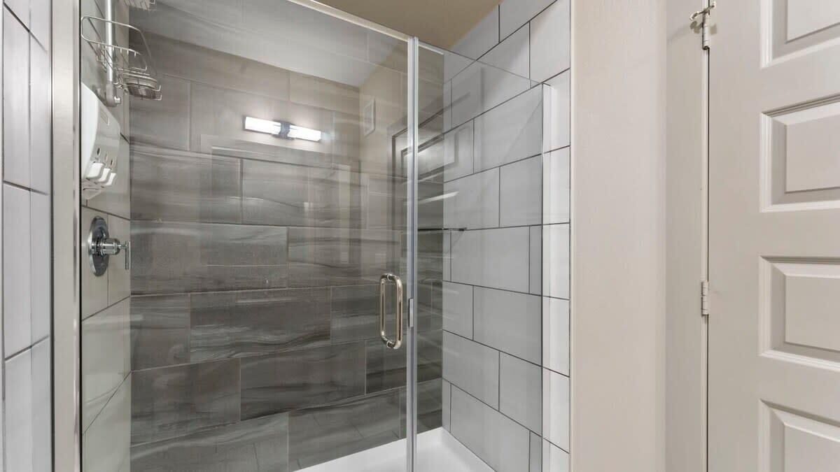 A glass-enclosed shower with a handle, tiled walls, and a white door.