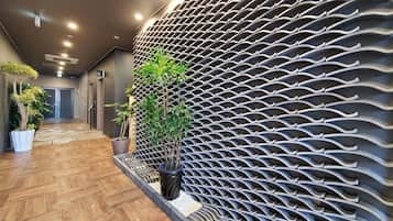 A hallway with a patterned wall, potted plants, and a wooden floor.