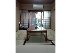Une pièce de style japonais traditionnel, avec un sol recouvert de tatamis, une table en bois, des portes coulissantes et un appareil de climatisation.