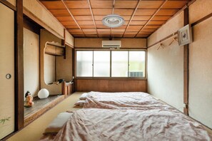 Una habitación japonesa tradicional con suelo de tatami, techo de madera y un ventanal grande.