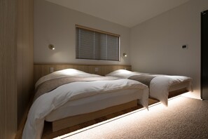 Une chambre avec deux lits, une fenêtre avec des stores et un luminaire fixé au mur.