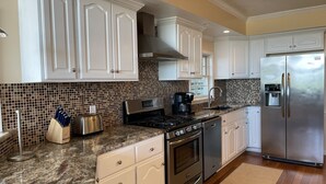 A modern kitchen with white cabinetry, a granite countertop, a stainless steel refrigerator, and a coffee maker.