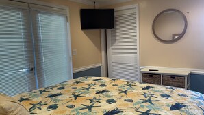 A bedroom with a bed, a television, a mirror, and a closet with sliding doors.