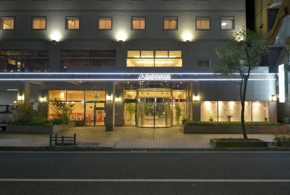 Hotel entrance with a glass door and stairs leading up to it, set on a street with a sidewalk.